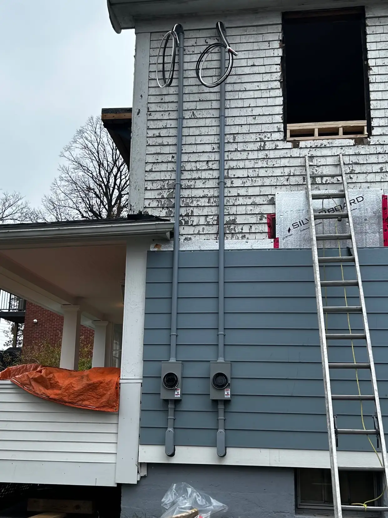 Twin service masts run up a two-storey house mid-renovation with the siding part finished