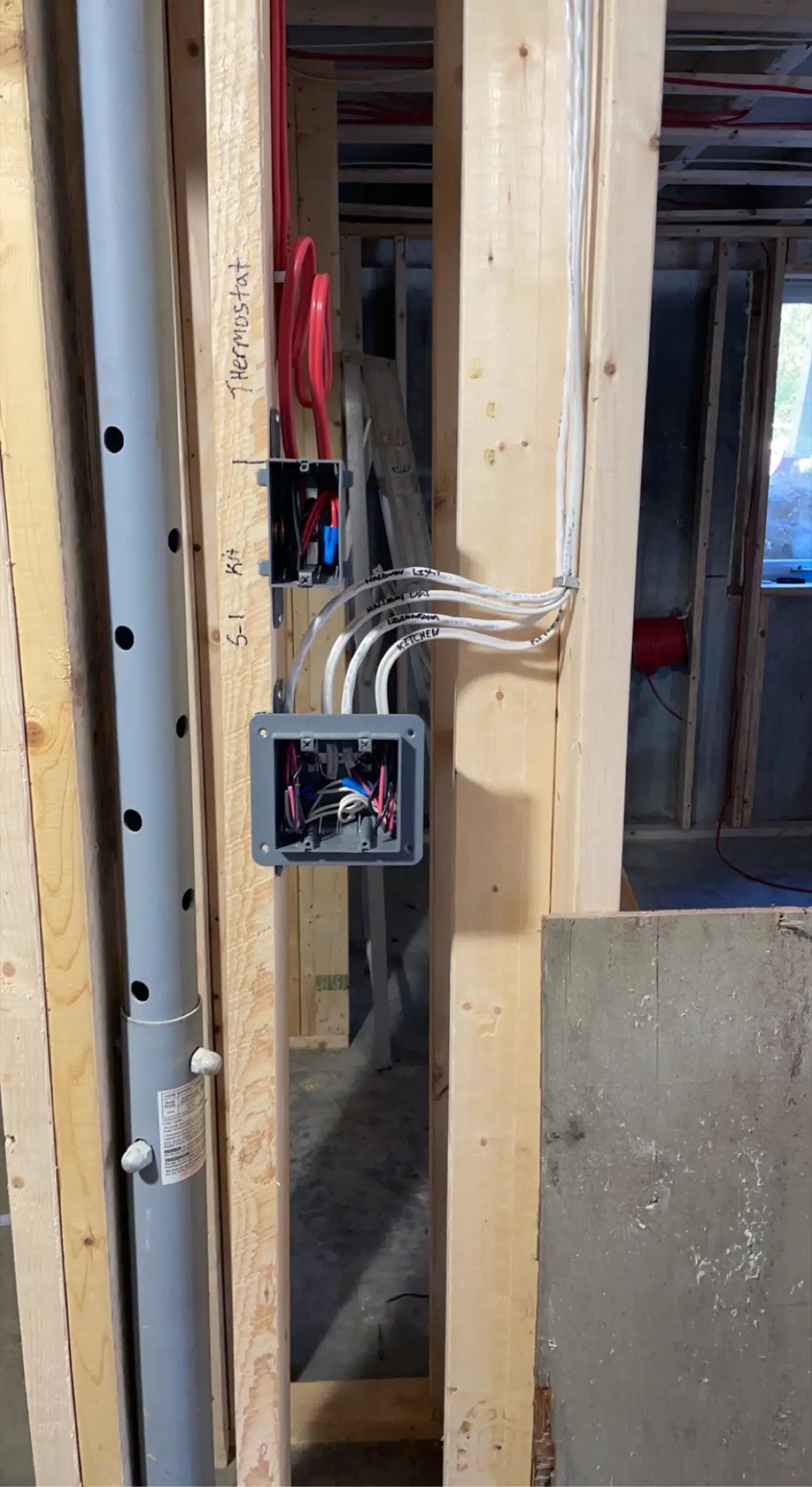 Rough-in box and thermostat cable labelled on framing in a basement build