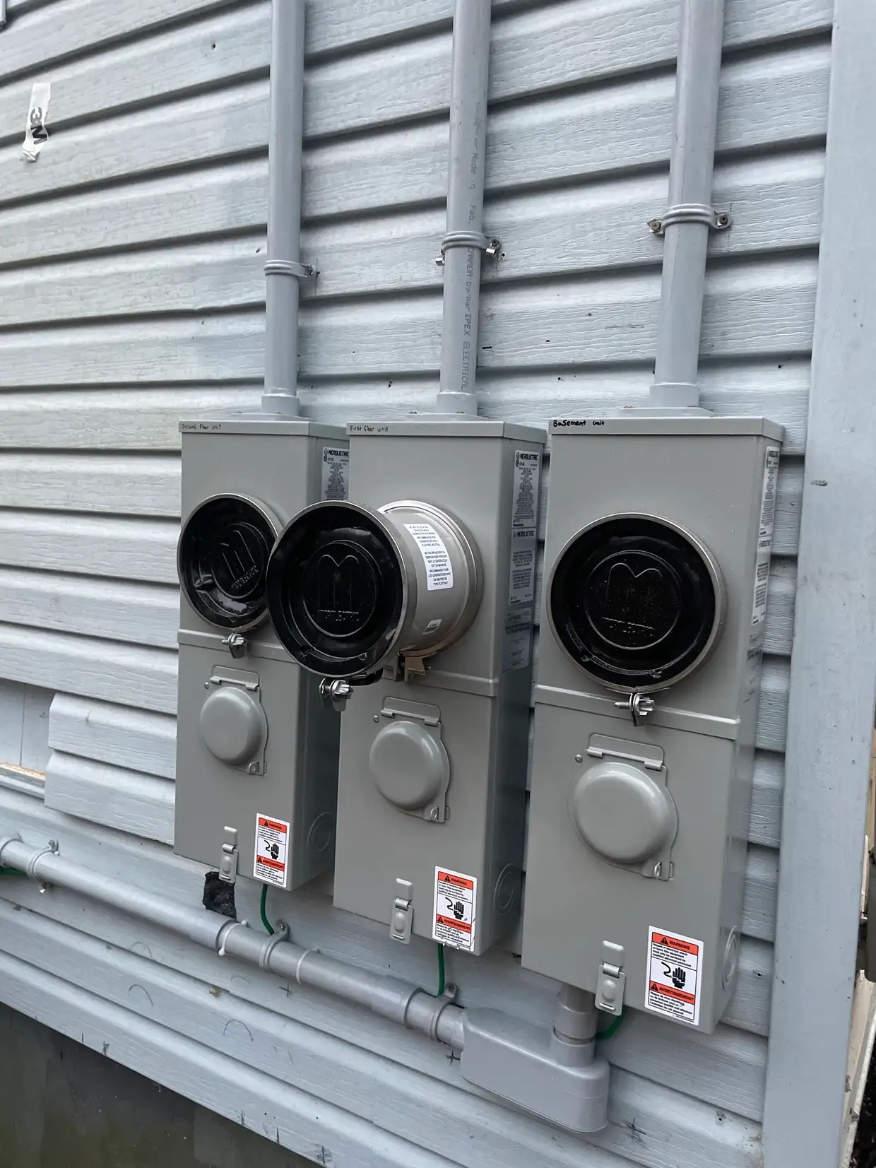 Three meter bases installed in a row and labelled by unit on a multi-unit building