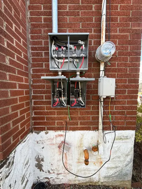 Two disconnects and a splitter wired at the meter on a brick wall during a service upgrade